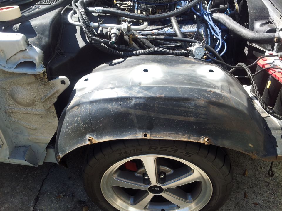 Close-up of a car's engine bay, showing the inner fender well and tire. Some wiring and engine components are visible