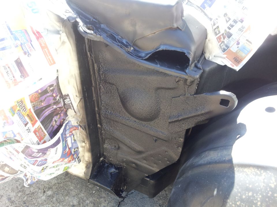 Close-up of vehicle frame being undercoated, with newspaper used for masking