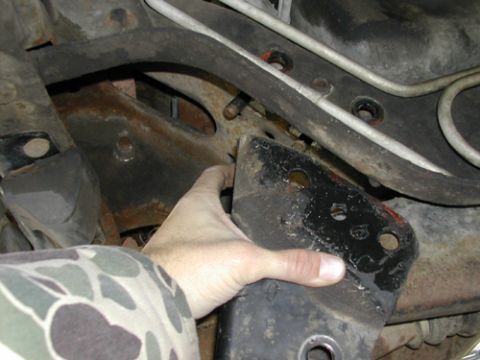 1996 Ford Bronco - A hand holds a black bracket against the rusty undercarriage of a vehicle, showing suspension components.