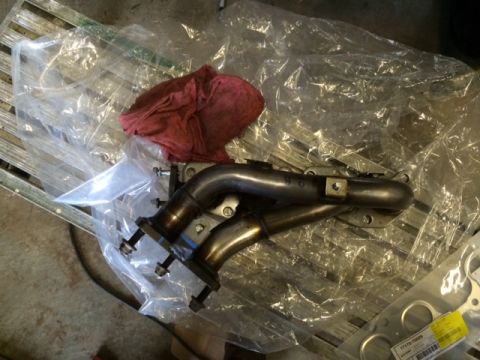 1988 Suzuki Samurai - Exhaust manifold part shown with a red rag and plastic wrap on a metal surface.