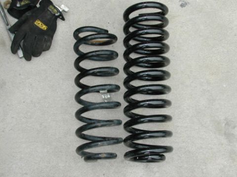 1996 Ford Bronco - Two black coil suspension springs and a pair of black work gloves with yellow logos are laid out on a textured surface.