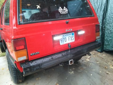 1986 Ford Bronco - The rear of a red Jeep Cherokee is visible, showing its license plate and a '4.0 Litre HIGH OUTPUT' badge.