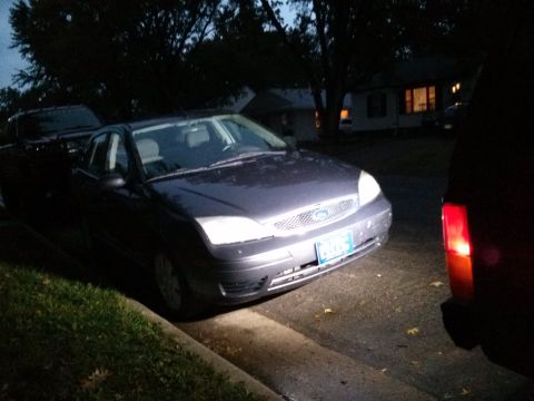 1986 Ford Bronco - A dark sedan is parked on the street at night, its headlights and grille clearly visible.