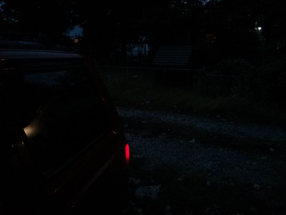 Darkness obscures most of a vehicle, only its red taillight is clearly visible
