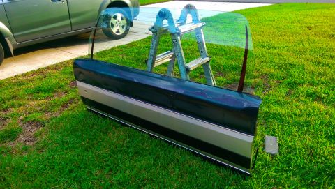 1996 Ford Bronco - A detached car door rests on a grassy lawn next to a ladder, with another vehicle partially visible.