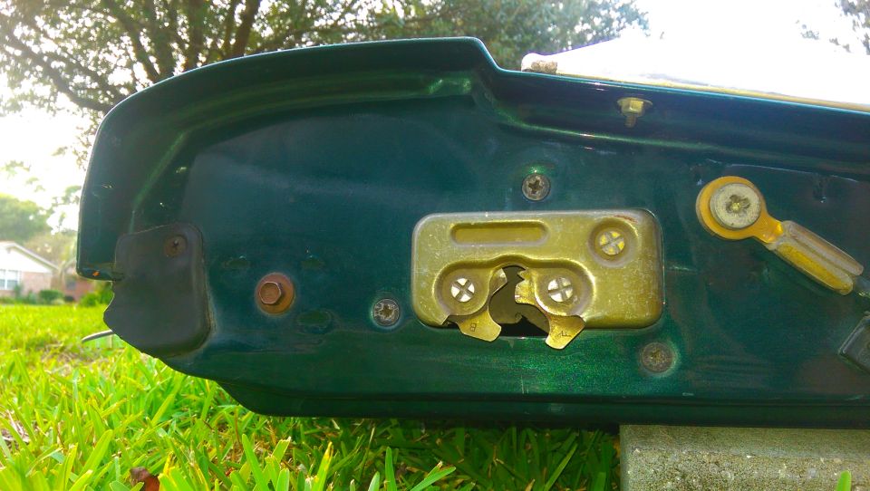 Close-up of a green tailgate's interior latch mechanism with visible screws and a yellow lever