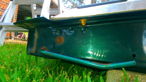 1996 Ford Bronco - Close-up of a green metallic car part with visible rust and a metal bar attached.