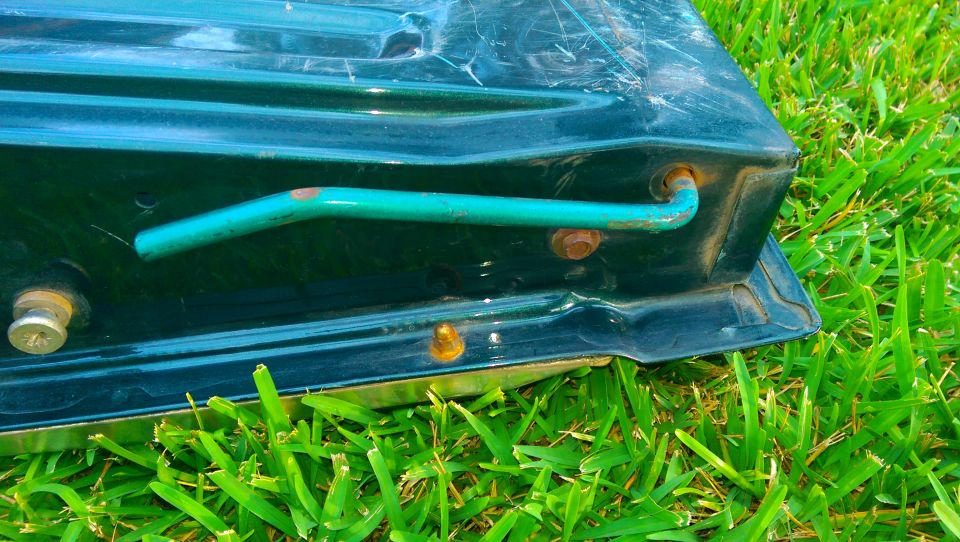 Painted sheet metal panel with mounting bolts and a teal tube lying on grass