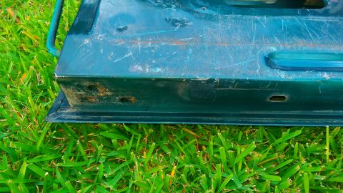 1996 Ford Bronco - The bottom edge of a green vehicle door shows scratches and wear, resting on green grass.