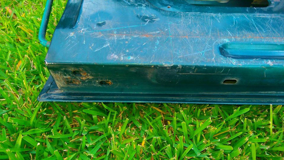Close-up of a green vehicle door's bottom edge with grass in the background