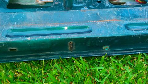 1996 Ford Bronco - Close-up of a green vehicle tailgate section showing wear and tear, with grass visible below.