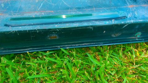 1996 Ford Bronco - Close-up of a green tailgate showing scratches and an oval cutout, resting on grass.