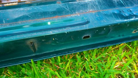 1996 Ford Bronco - The lower edge of a green vehicle door, with visible wear and tear, rests on grass.