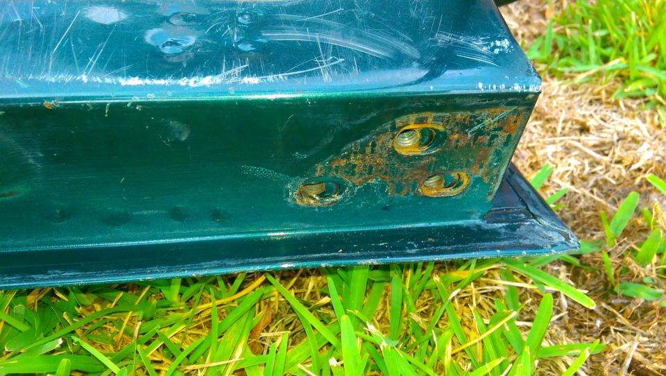 Green tailgate corner showing rust around bolt holes and scratches on the paint