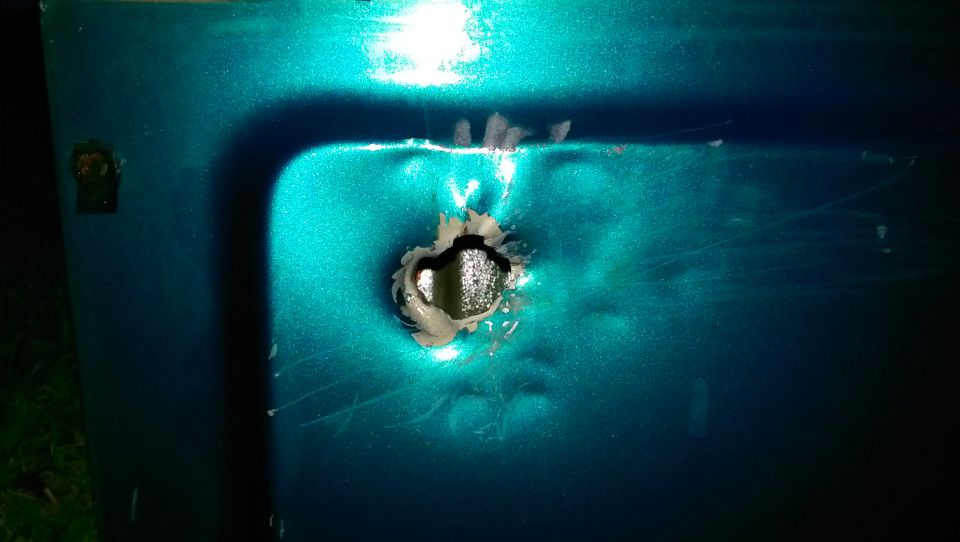 Teal car door with a large hole punched through it, showing damage and rust