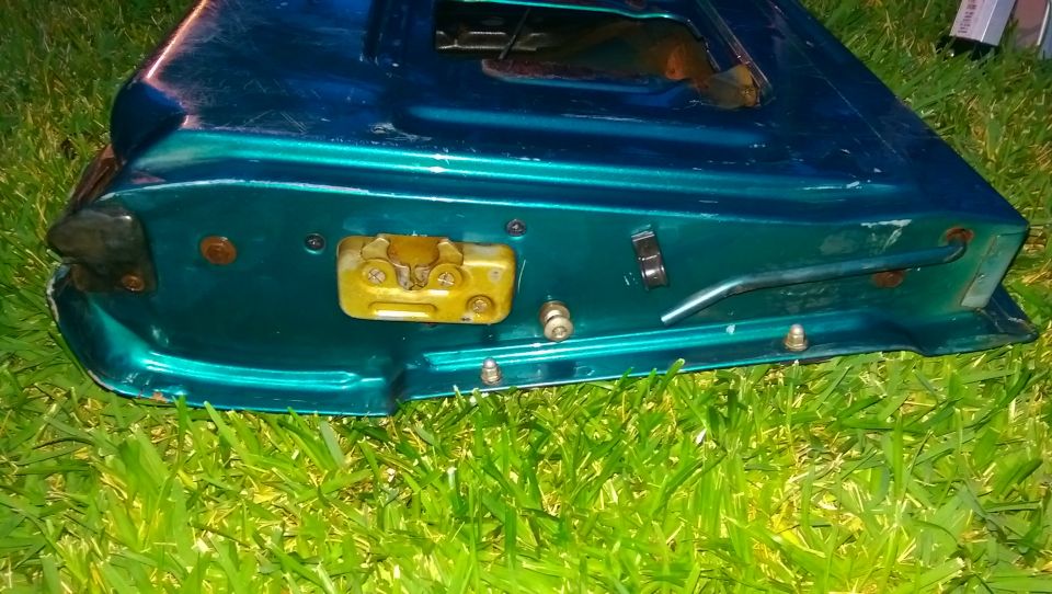 Teal tailgate latch mechanism with yellow striker plate and metal handle on grass