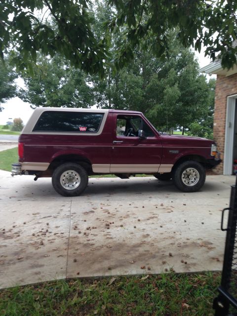 1996 Ford Bronco - A side view of a maroon and tan Ford Bronco with aftermarket wheels and a lift kit.