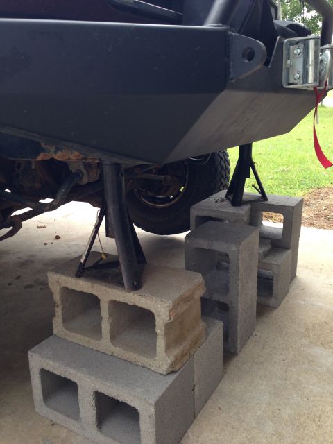 1996 Ford Bronco - The rear bumper of a vehicle is elevated by jack stands and cinder blocks, suggesting maintenance or modification work.