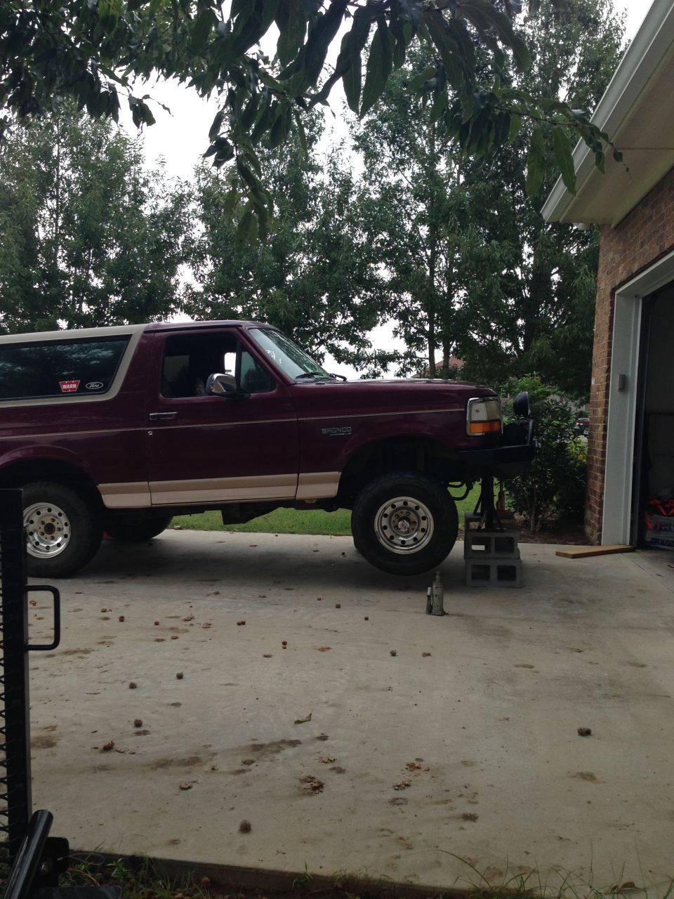 Maroon Ford Bronco on jack stands in front of a garage