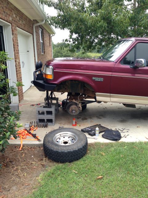 1996 Ford Bronco - Maroon 1996 Ford Bronco undergoing lift kit installation, with front end elevated and parts laid out.