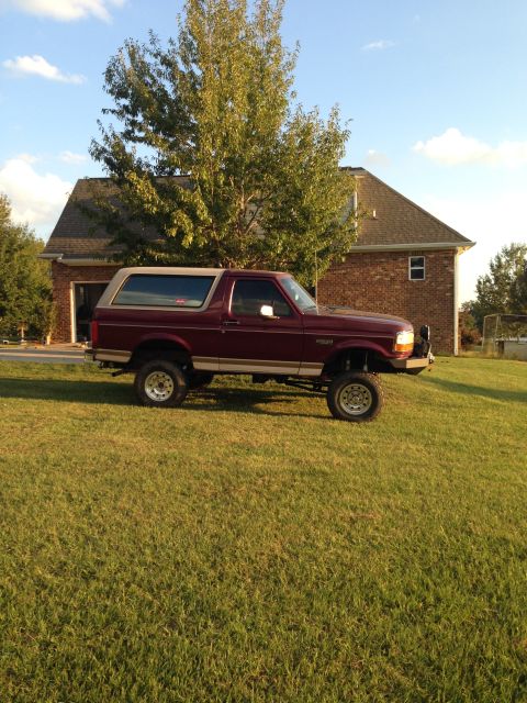 1996 Ford Bronco - This lifted 1996 Ford Bronco is shown in a side profile view, parked on a grassy incline with a house in the background.