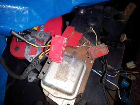 1976 Ford Ranchero - Close-up view of automotive electrical components, including a red battery, voltage regulator, and various red connectors and wiring.
