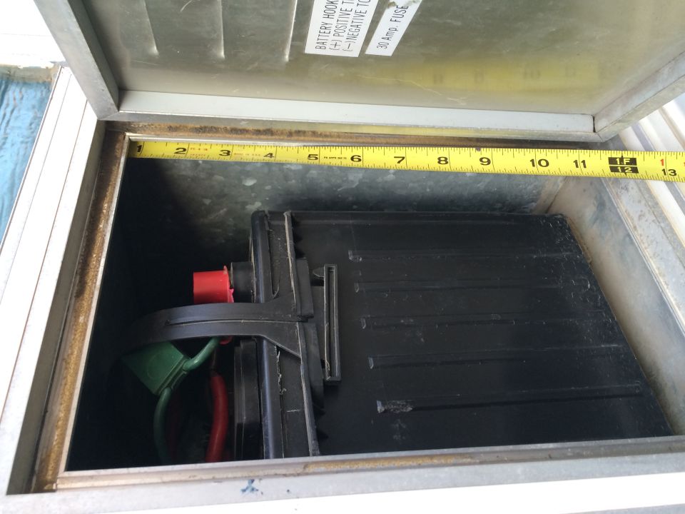 Battery box with battery and cables inside. Tape measure shows dimensions