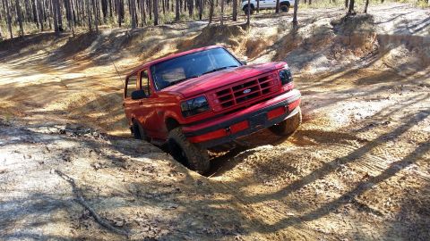 1995 Ford Bronco - Red 1995 Ford Bronco tackling challenging terrain off-road, with another vehicle in the distance.