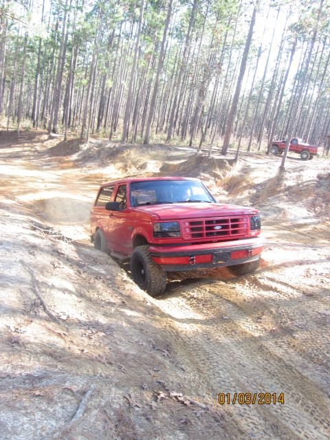 1995 Ford Bronco - A red 1995 Ford Bronco navigates a challenging off-road trail with another vehicle in the distance.