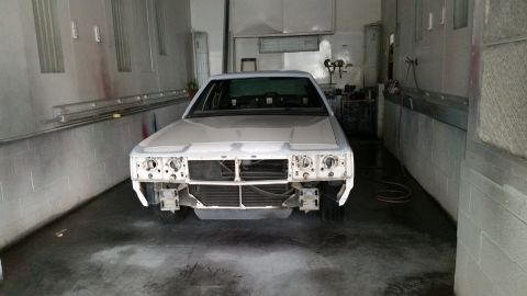 1991 Ford LTD Crown Victoria - A white sedan is in a paint booth, awaiting restoration, with its front end disassembled.