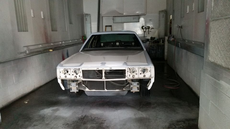 White sedan in paint booth, front view, missing headlights and grille