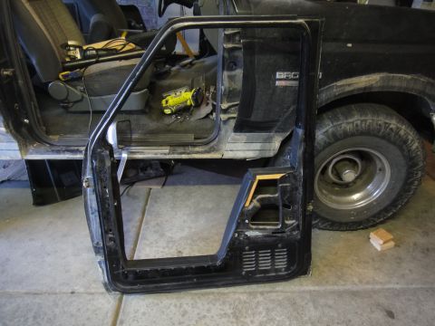1988 Ford Bronco - The driver's side door of a 1988 Ford Bronco is removed, revealing the interior and the vehicle's exterior.