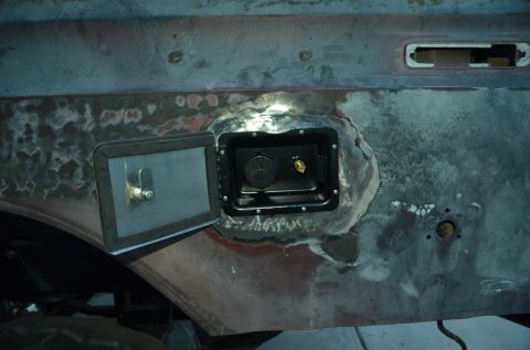 1979 Ford Bronco - Close-up view of an open fuel filler door with cap and brass fitting visible on the vehicle's body.