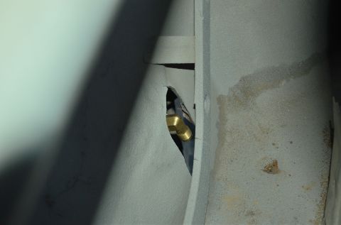 1979 Ford Bronco - A close-up view shows a brass fitting connected to a black hose, passing through an opening in a gray metal surface.