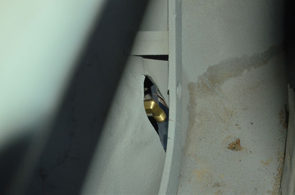 Brass fitting and black hose visible through a hole in a gray metal panel
