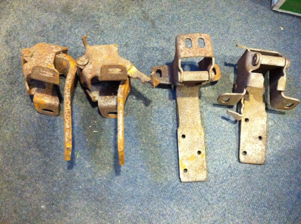 Four rusty door hinges with springs and mounting straps laid on blue carpet