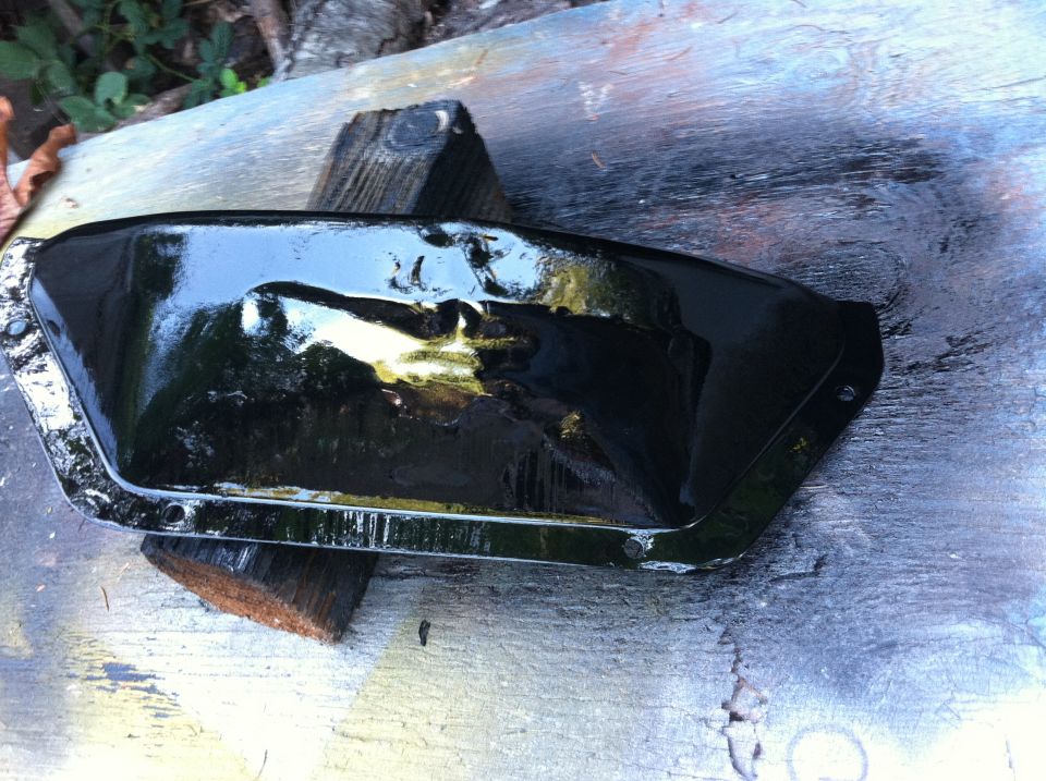 Black oil pan resting on wood blocks, with a Supermotors logo at the bottom right