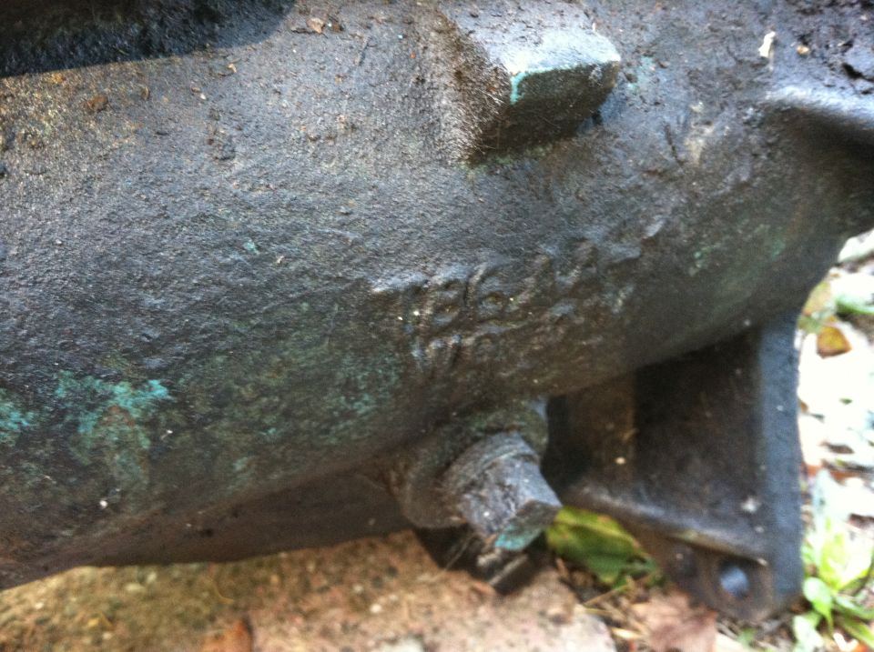 Close-up of a greasy, cast-iron engine component with visible casting numbers stamped into the metal