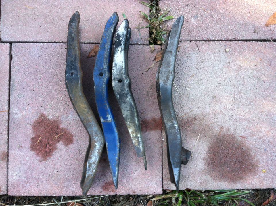 Four curved metal car parts, one painted blue, laid on brick pavers