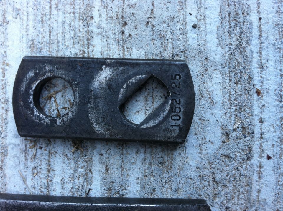 Close-up of a metal bracket with a circular hole and a square hole, marked with '1-052725'