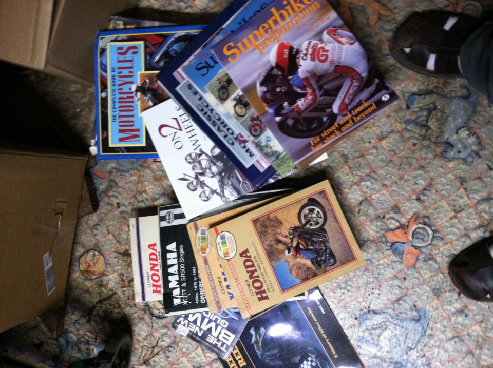 Pile of motorcycle repair manuals including Honda, Yamaha, and BMW, on a patterned carpet