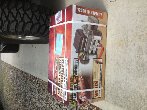 1996 Ford Bronco - Boxed Badland 12000 lb capacity off-road winch with cable, next to a vehicle tire.