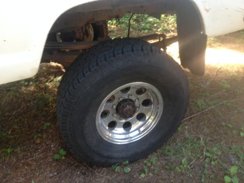 1971 Ford F-250 - Close-up view of the rear wheel and fender assembly of a white truck, showing its suspension and tire.