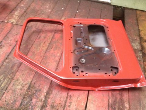 1971 Ford F-250 - A red truck door, showing its interior structure, rests on a weathered wooden floor.