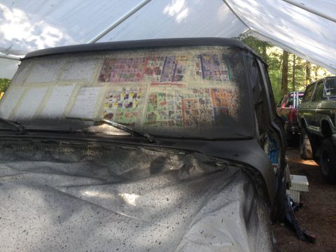 1971 Ford F-250 - A truck's windshield is covered with taped-up pages, possibly for masking or decoration, while parked under a tarp with other vehicles near…