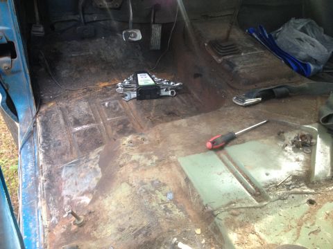 1971 Ford F-250 - The interior floor of a truck shows significant rust and wear, with tools laid out for work.