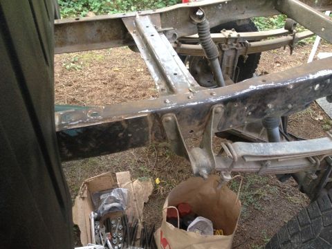 1971 Ford F-250 - Bare painted truck frame with leaf springs and steering components during restoration, parts bags on the ground.