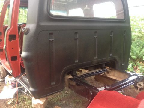 1971 Ford F-250 - The rear of a red truck cab and black bed is visible, with the truck supported by blocks.