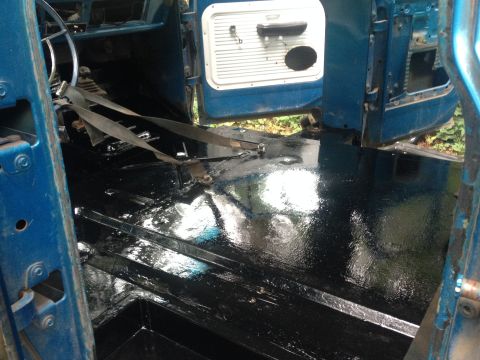 1971 Ford F-250 - Interior cab floor of a blue truck freshly coated in glossy black, with seatbelt and access panel visible.
