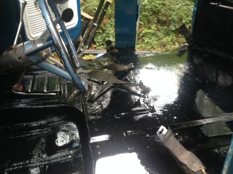 1971 Ford F-250 - The shiny black floor of a vehicle interior, with the steering column and seat belt anchors visible.